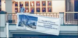  ?? J. SCOTT TRUBEY / AJC ?? A worker at Atlanta City Hall hangs a banner promoting March as National Purchasing Month. Most contractor­s are supporting one mayoral candidate.