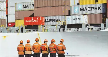  ??  ?? STANDOFF: Chinese workers stand in front of a loaded cargo ship docked at a port in Qingdao yesterday.