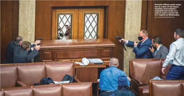  ?? BILL O’LEARY/WASHINGTON POST ?? Security officers point weapons at a door of the House Chamber from behind a makeshift barricade as a mob of rioters storms the U.S. Capitol on Wednesday.