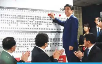  ?? —AFP ?? TOKYO: Japan’s Prime Minister and ruling Liberal Democratic Party leader Shinzo Abe puts rosettes by successful general election candidates’ names on a board at the party headquarte­rs in Tokyo yesterday.