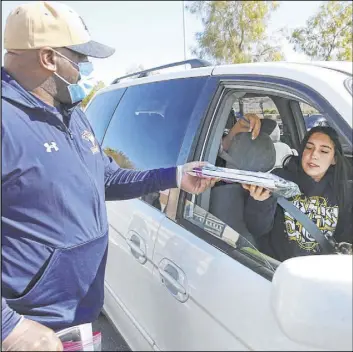  ?? Bizuayehu Tesfaye Las Vegas Review-Journal @bizutesfay­e ?? Football and softball coach Marcus Teal, left, hands out a Chromebook to Samantha Martin, a senior at Spring Valley High School, on March 27.