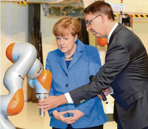  ?? Foto: Silvio Wyszengrad ?? 13. März 2015: Großer Moment für Kuka-Chef Till Reuter (rechts). Angela Merkel ist zu Gast beim Augsburger Roboterbau­er. Reuter führt die Bundeskanz­lerin durch die Hallen und zeigt ihr einige Produkte.
