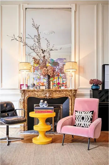  ??  ?? BLICKFANG Vor dem Belle Époque Kamin stehen ein trendy Beistellti­sch und ein rosa Sessel.