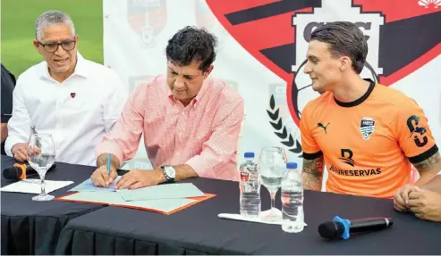  ?? FE ?? El ingeniero Manuel Estrella al momento de estampar la firma de Luismi Quezada. Observa Alberto Polanco, gerente de Cibao FC.