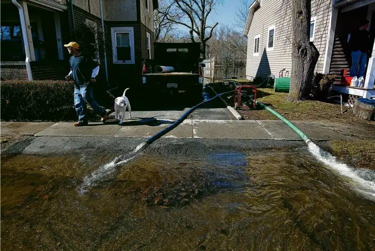  ?? YOON S. BYUN/GLOBE STAFF/FILE 2010 ?? Paul Welliver walks his dog, Bubba, in front of a house as his neighbors pump out their water-filled basements in Winchester after three days of nonstop rain in 2010.