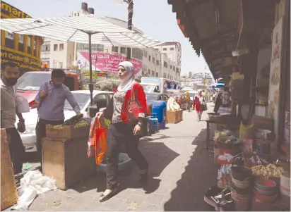  ?? (Mohamad Torokman/Reuters) ?? A WOMAN WALKS past shops in Ramallah earlier this year.