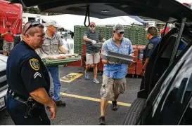  ?? Michael Ciaglo / Houston Chronicle ?? Operation BBQ Relief volunteer Brandon Reyes, center, packs barbecue into the back of a police car for delivery in Houston. The volunteer pitmasters aim to feed at least half a million people over the course of the next two weeks.