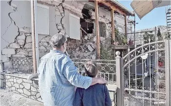  ?? — AFP photo ?? A father and son look at a damaged at a house in the village of Damasi, near the town of Tyrnavos, after a strong 6,3magnitude earthquake hit the Greek central region of Thessaly.