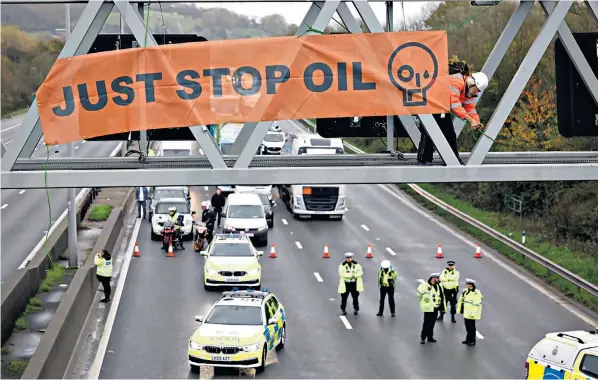  ?? ?? A Just Stop Oil activist clambers on to a gantry above the M25. The protest was repeated at 13 separate locations on the 116-mile orbital and caused gridlock during the rush hour on what is Britain’s busiest motorway