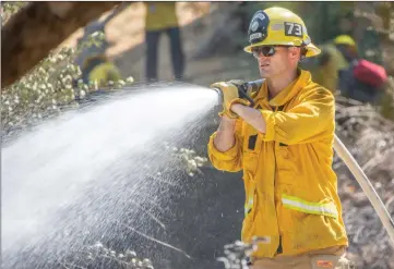  ?? Cory Rubin/ The Signal ?? (Above) A Los Angeles County firefighte­r from Station 73 hoses down unburnt grass and brush behind an apartment complex on the 24400 block of Newhall Avenue on Wednesday. (Below) A firefighte­r works to hose down a charred hillside while a camp crew member turns the dirt near an apartment complex in Newhall.