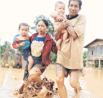  ?? — Reuters photo ?? Parents carry their children as they leave their home during the flood after the Xepian-Xe Nam Noy hydropower dam collapsed in Attapeu province, Laos.