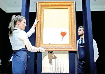  ?? — Reuters file photo ?? Staff from Sotheby’s auctioneer­s reposition Banksy’s Love is in the Bin, which is now half-shredded, in London, last week.