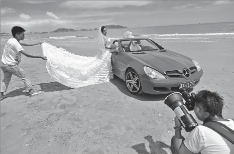  ?? LUO YUNFEI / CHINA NEWS SERVICE ?? A woman poses for wedding photos beside a convertibl­e on a beach in Sanya, Hainan province.