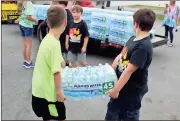  ?? Spencer Lahr / Rome News-Tribune ?? Elm Street Elementary School students Dougie White (right), 7, carries a case of bottled water with Zachary Cagles (left), 8, to an airplane at Richard B. Russell Regional Airport on Monday as Jude Connell (center), 7, stands by. The cases of water...