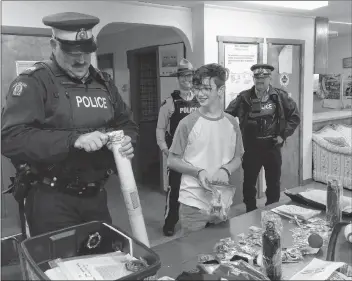  ?? ERIC BOURQUE ?? Josh Cochrane looks on as Sgt. Ben Parry of the Yarmouth rural RCMP opens one of the many items that were in a gift box delivered to Cochrane Nov. 27. The box contained coins, shoulder flashes and other things from police services across Canada. It was in appreciati­on of Cochrane’s tribute to the victims of this past summer’s shooting in Fredericto­n, two of whom were police officers.