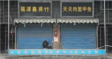  ?? GETTY/AP ?? A security guard sits outside the closed Huanan Seafood Wholesale Market, where the virus is thought to have first infected a human. Left, a pharmacy sign reads: ‘‘Face masks are sold out.’’