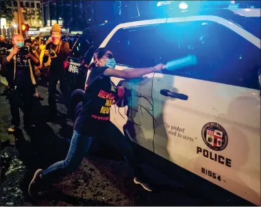  ??  ?? ATTACK: A woman demonstrat­or wearing a face mask takes aim at a police car in downtown Los Angeles