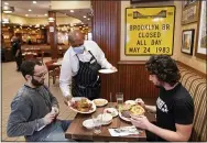  ?? MARK LENNIHAN — THE ASSOCIATED PRESS FILE ?? On Sept. 30, 2020, Waiter Lenworth Thompson serves lunch to David Zennario, left, and Alex Ecklin at Junior’s Restaurant in New York.