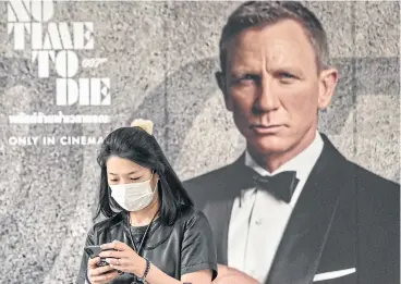  ??  ?? A woman wearing a facemask walks past a poster for the new James Bond movie No Time To Die in Bangkok.