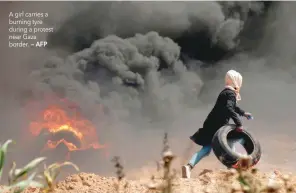  ??  ?? A girl carries a burning tyre during a protest near Gaza border. — AFP