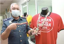  ?? — Bernama photos ?? Law shows the participat­ion medal and T-shirt for the 2016 Bomba charity run, during the interview at his office.