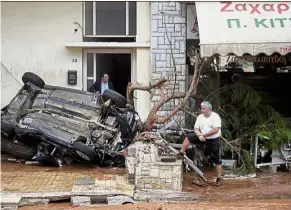  ??  ?? Badly hit: Men standing next to an overturned car following flood-causing rainfall in the town of Mandra, Greece. — Reuters