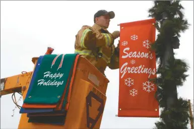  ?? Kevin Myrick/ SJ ?? Cedartown firefighte­r Nick Demko hangs garland and signs from light poles on Main Street ahead of the holiday season. Check out Page 21A for more informatio­n about Cedartown’s festivitie­s.