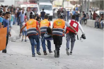  ??  ?? Palestinia­n paramedics carry a man injured during clashes between demonstrat­ors and Israeli security forces at the Qalandiya checkpoint, between Ramallah and Jerusalem, in the occupied West Bank. (AFP)