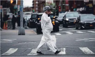  ?? JOHANNES EISELE AFP/GETTY IMAGES ?? A pregnant woman wearing a haz-mat suit walks in New York City on Monday. The Centers for Disease Control listed six new symptoms of COVID-19 on its website on April 18.