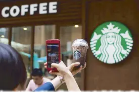  ?? AFP ?? A woman takes a picture of her beverage at a Starbucks coffee shop in Beijing on Friday.