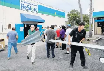  ?? MIKE STOCKER/STAFF PHOTOGRAPH­ER ?? Jonathan Iovino of Boca Raton and Omar Torres of Miami load up on hurricane shutters from the Habitat for Humanity ReStore on Broward Boulevard, where there was a line out the door to buy them Tuesday.