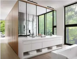  ??  ?? BOTTOM A wall unit housing walk-in closets and additional storage divides the master ensuite from the sleeping quarters. The shower wall, reflected in the quartz-topped vanity’s mirrors, is clad in titanium – a direct reference to the front exterior wall. Soaker tub from Taps; faucets by Watermark.