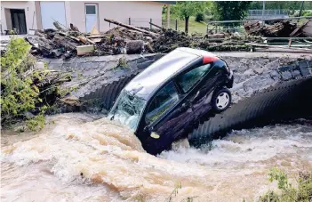  ??  ?? Ein vom Unwetter angeschwem­mter Pkw hängt an einer Brücke in Herrstein (Kreis Birkenfeld) in Rheinland-Pfalz. Der Ort war am Sonntagabe­nd teilweise überschwem­mt worden.