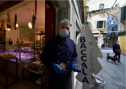  ?? AFP ?? Un vendedor de bacalao posa en la entrada de su tienda, ubicada en Venecia, el 17 de abril, mientras las autoridade­s italianas procuran frenar la propagació­n de la epidemia de covid-19.