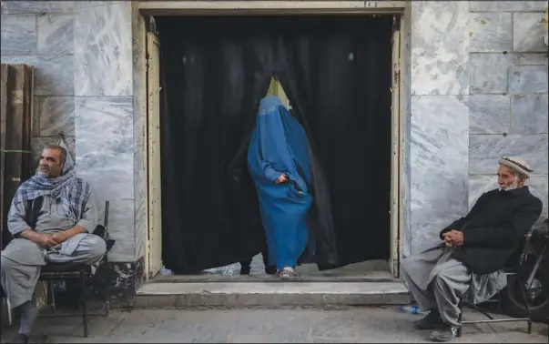  ?? (AP/Bram Janssen) ?? A woman leaves a Shiite shrine Nov. 9 in a predominan­tly Hazara neighborho­od while two men stand guard in Kabul, Afghanista­n.