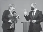  ?? MARKUS SCHREIBER/AP ?? Outgoing Chancellor Angela Merkel accepts flowers from new leader Olaf Scholz during a handover ceremony in Berlin Wednesday.