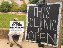  ?? ASSOCIATED PRESS ?? An anti-abortion supporter sits behind a sign that advises the Jackson Women’s Health Organizati­on clinic is still open in Jackson, Miss., in 2022.
