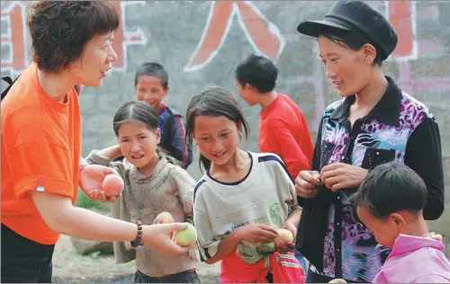  ?? PHOTOS PROVIDED TO CHINA DAILY ?? Zhang Junlan gives peaches to children at a village in Liangshan, Sichuan province, during one of her many trips to the remote area.