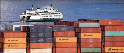  ?? AP/ELAINE THOMPSON ?? A Washington state ferry passes a loaded container ship anchored in Elliott Bay near downtown Seattle last month.