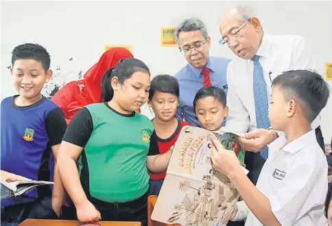  ??  ?? Mahdzir (right) goes through a book with pupils during a visit to SK St Martin Merdang.