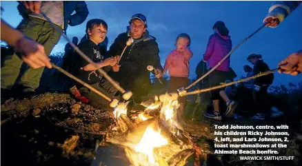  ?? WARWICK SMITH/STUFF ?? Todd Johnson, centre, with his children Ricky Johnson, 4, left, and Lara Johnson, 2, toast marshmallo­ws at the Ahimate Beach bonfire.