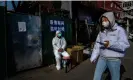  ?? Photograph: Kevin Frayer/Getty Images ?? A woman wears a mask as she walks by an epidemic control worker as outside a locked-down community in Beijing.