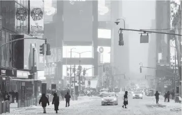  ?? MARY ALTAFFER AP ?? Visitors make their way through New York’s Times Square during a snow storm on Saturday. A powerful nor’easter swept up the East Coast this weekend, threatenin­g to bury parts of 10 states under deep, furiously falling snow accompanie­d by coastal flooding and high winds that could cut power and leave people shivering in the cold weather.