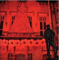  ??  ?? Thousands of knitted poppies forming a backdrop to the memorial sculpture of a Durham Light Infantry Soldier outside Durham Town Hall which has also been illuminate­d red for Remembranc­e Day.