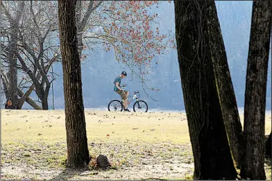  ?? Arkansas Democrat-Gazette/THOMAS METTHE ?? A cyclist checks his cellphone while riding along the river trail at Burns Park in North Little Rock on Thursday.