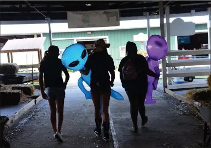  ?? TANIA BARRICKLO — DAILY FREEMAN ?? Three friends walk through the cattle barn at the Ulster County Fair in New Paltz, N.Y., on Tuesday, two of them holding inflatable aliens that were among prizes offered at game booths.