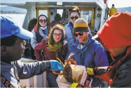  ??  ?? Truitt (left) gives passengers Julia Ersen (center, left) and Andrew Sutherland (center, right) their allotment of crabs for the day.