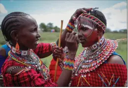  ?? ?? A Maasai woman paints the face of another Dec. 10 as they prepare to watch the Maasai
Olympics.