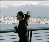  ?? The Canadian Press ?? The snow covered North Shore Mountains are seen in the background as a jogger runs along the waterfront in Vancouver.