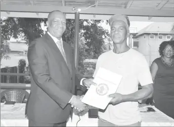  ?? (Ministry of the Presidency photo) ?? Minister of State Joseph Harmon (left) presents one of the ‘Permission to Occupy State Lands’ document to this gentleman from the community.